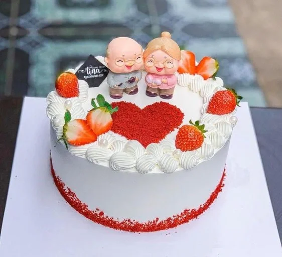 Mẫu bánh sinh nhật đẹp phủ kem trắng, trang trí dâu tây, trái tim đỏ và mô hình đôi nhân vật hoạt hình đáng yêu