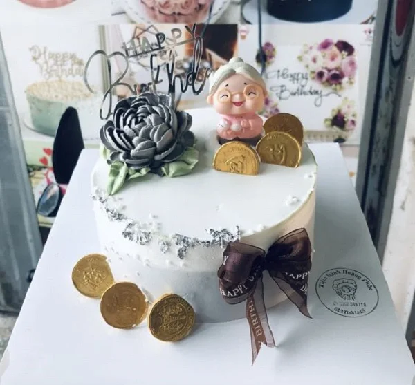 Mẫu bánh sinh nhật đẹp màu trắng trang trí hoa kem xám đen, tượng ông Thọ, đồng tiền vàng và nơ ruy băng sang trọng
