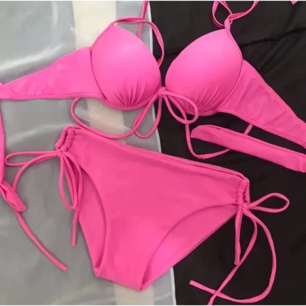 Bikini 2 mảnh màu hồng kiểu dây buộc được sắp xếp trên nền vải xám và đen.