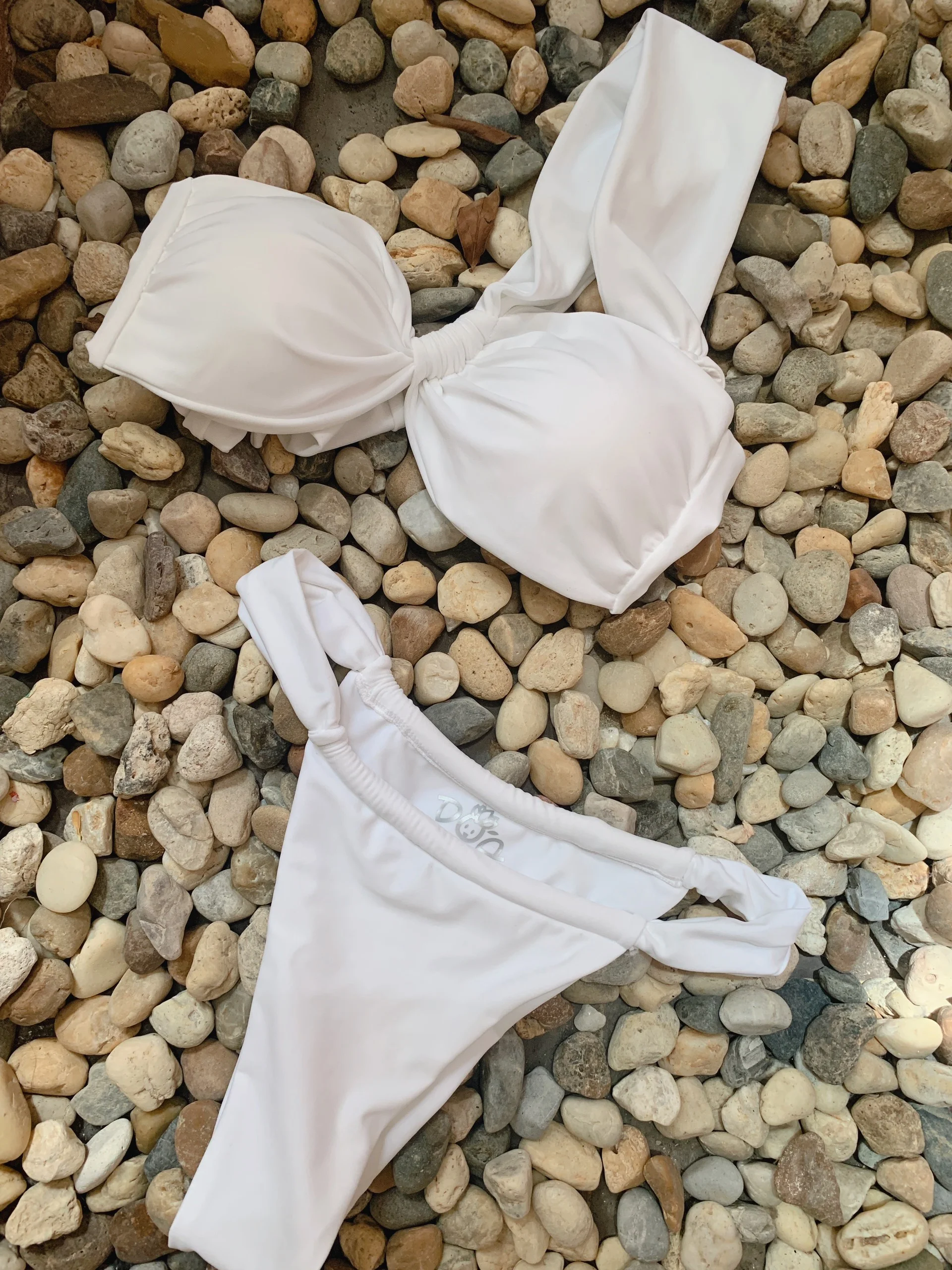 Bikini hai mảnh màu trắng đặt trên nền sỏi