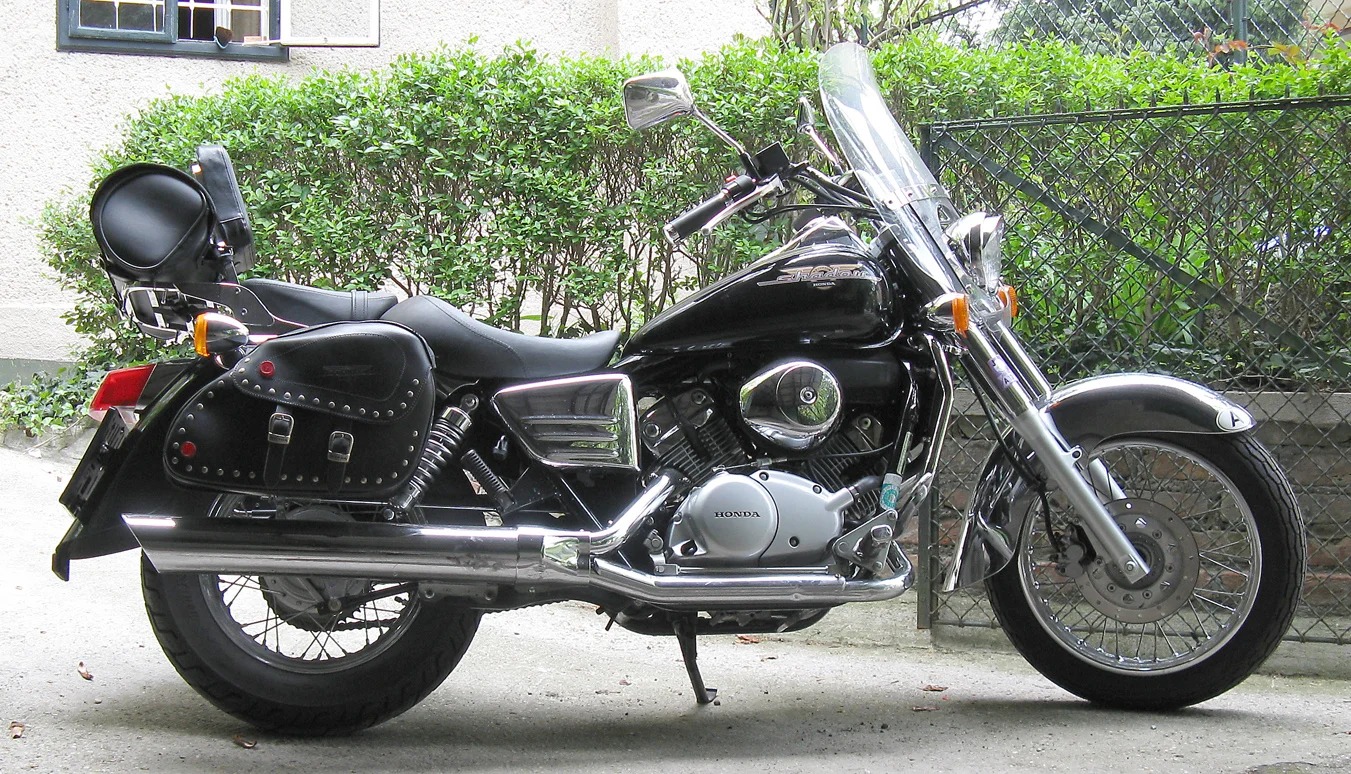 Ảnh meme hài bựa về chiếc mô tô cruiser Honda màu đen bóng đỗ trước hàng rào xanh