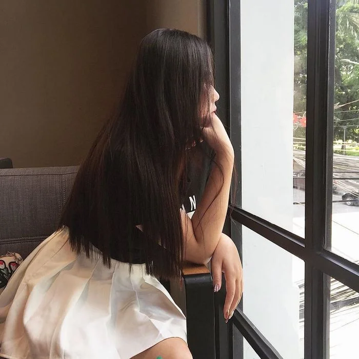 Cô gái tóc dài ngồi bên cửa sổ che mặt
