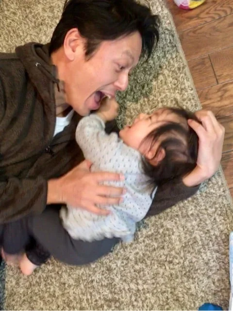 Hình nền meme người lớn chơi đùa với em bé trên thảm, cả hai tạo biểu cảm hài hước và đáng yêu